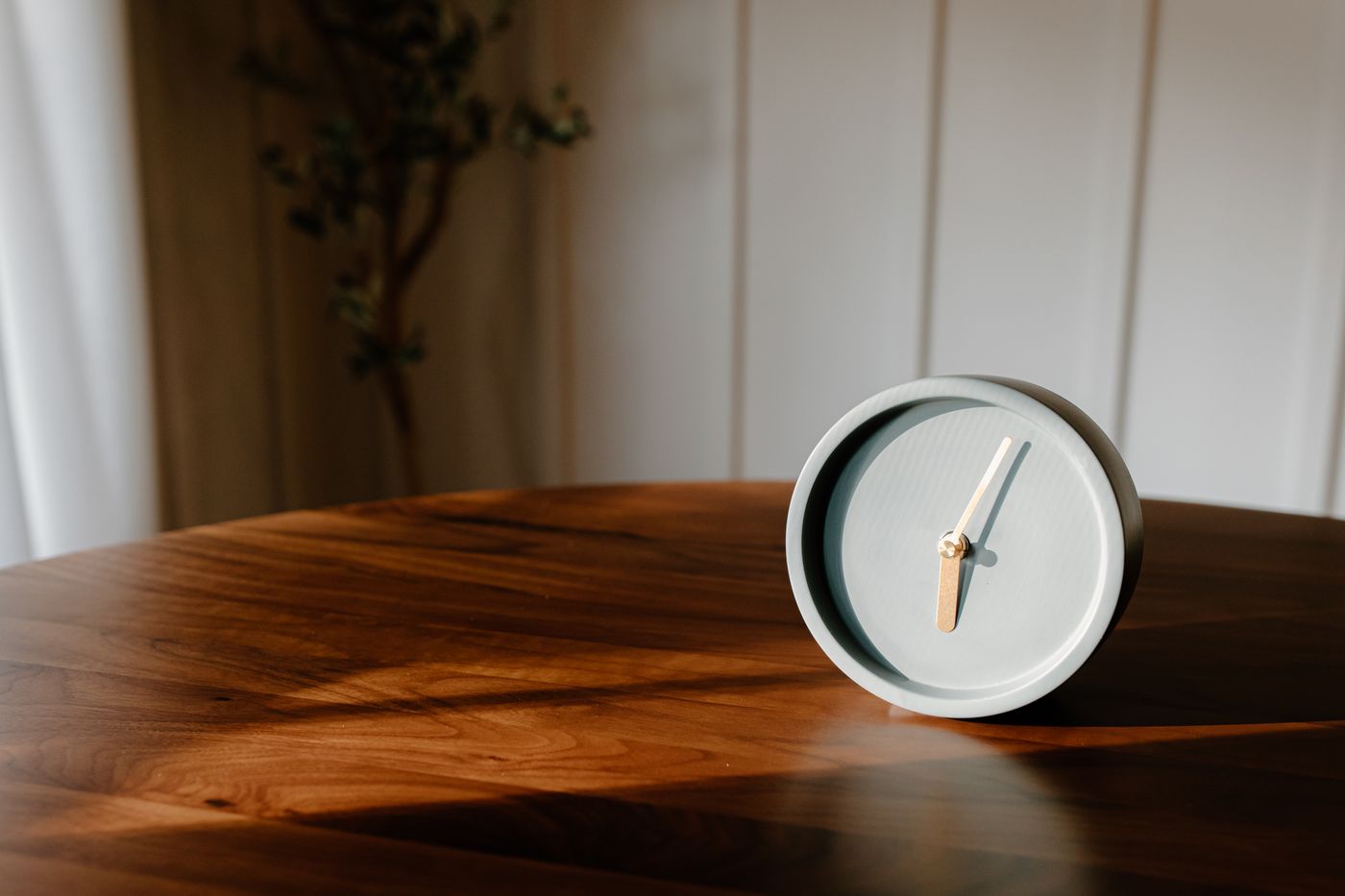 A minimalist grey tabletop clock in warm sunlight