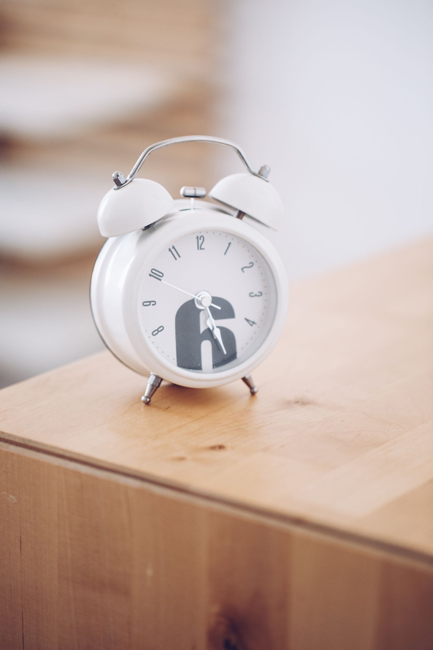 A white analogue alarm clock on a wooden bedside surface