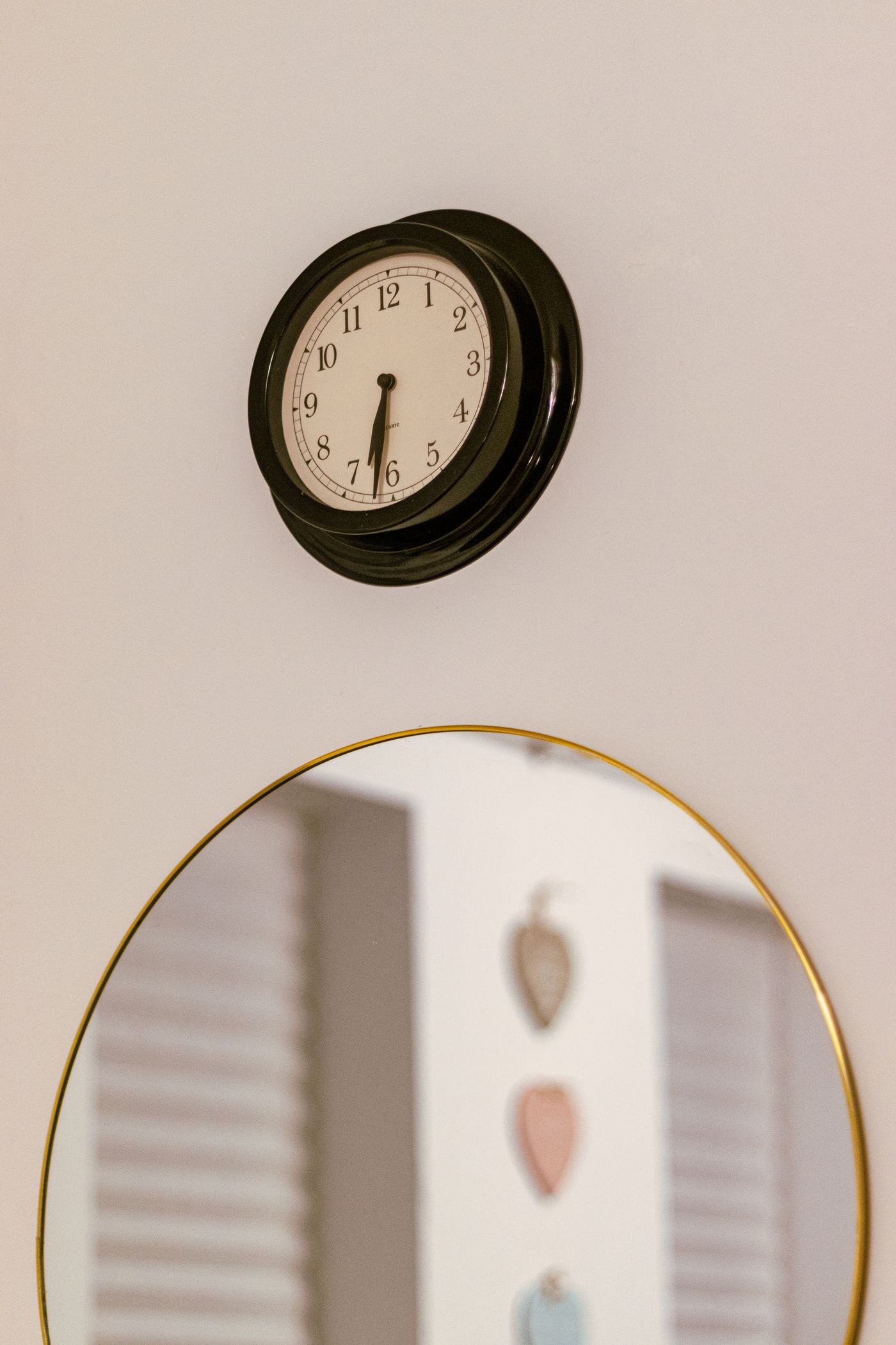 A round numbered clock hanging above a mirror