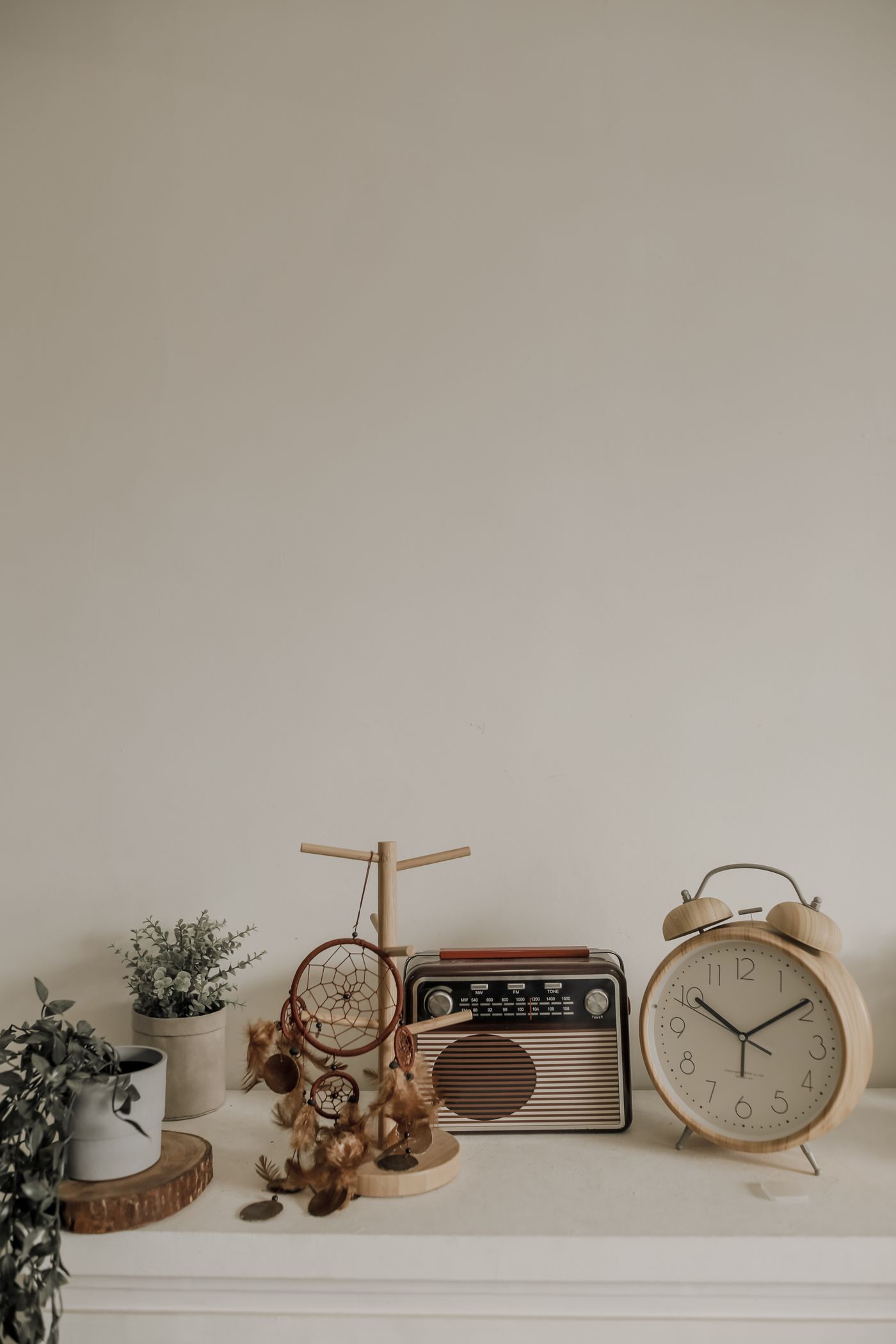 A small clock arranged on a shelf with a radio and plants