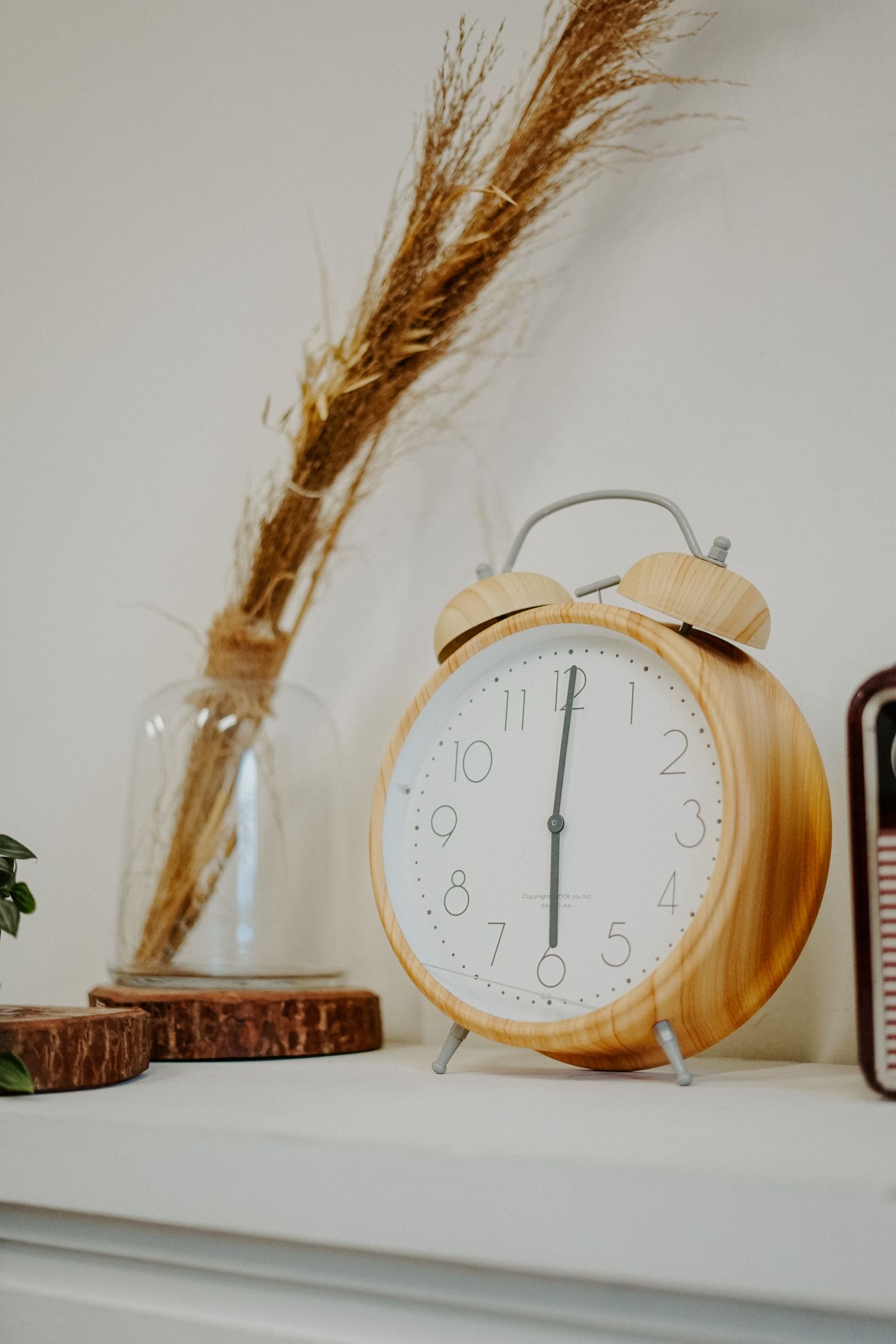 A wood-toned alarm clock displayed on a pale painted shelf