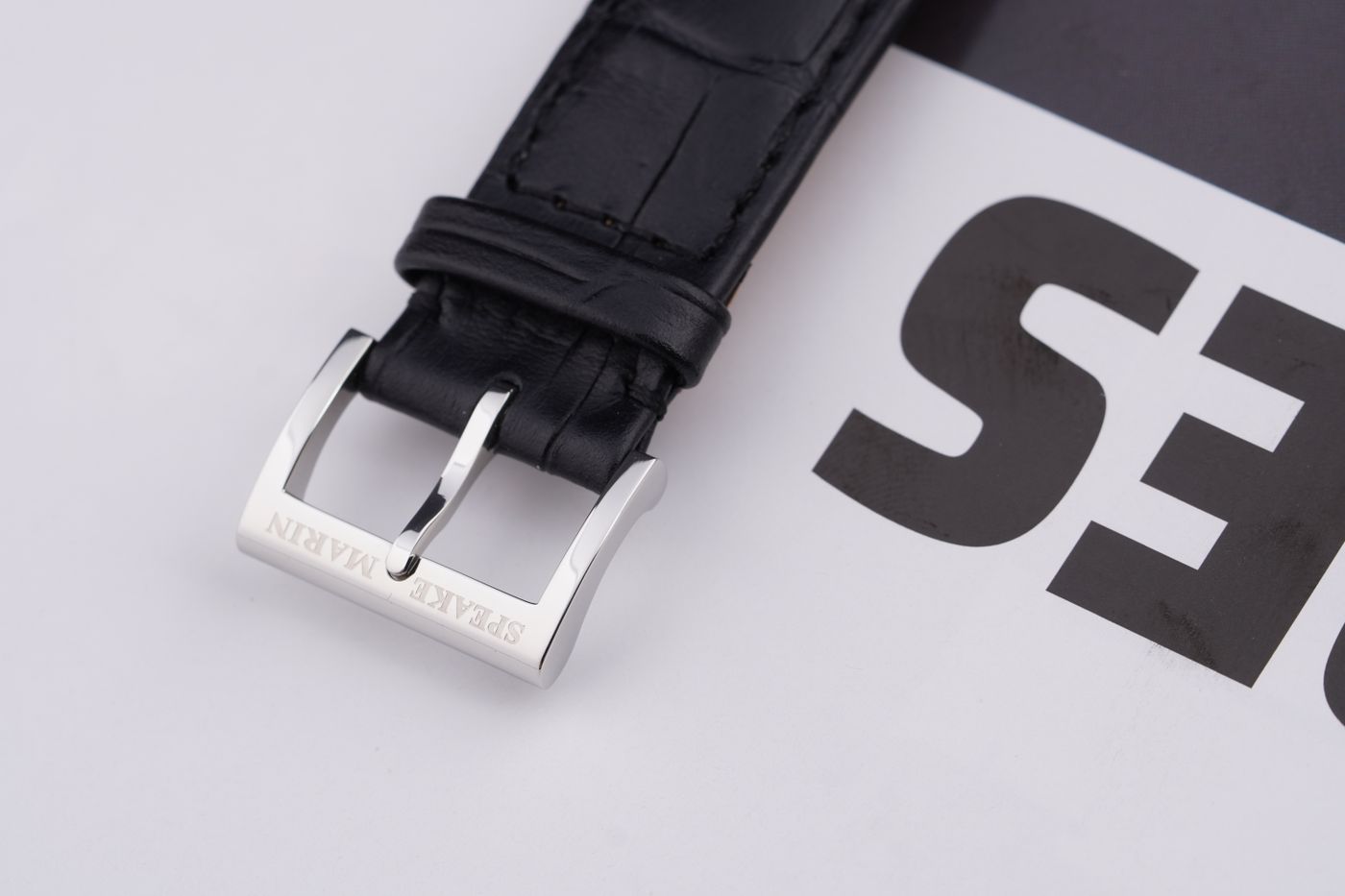 A close view of a silver buckle fitted to a black leather watch strap